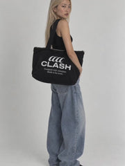 Model wearing the black Clash Foundation Tote Bag with embroidered logo, black tank top and baggy jeans in a minimalist studio.